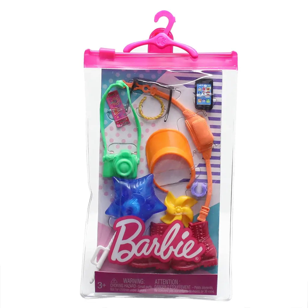 Barbie tourist fashion pack in clear case with orange visor, green camera, red boots, blue star balloon, and playful travel-themed accessories for dolls.