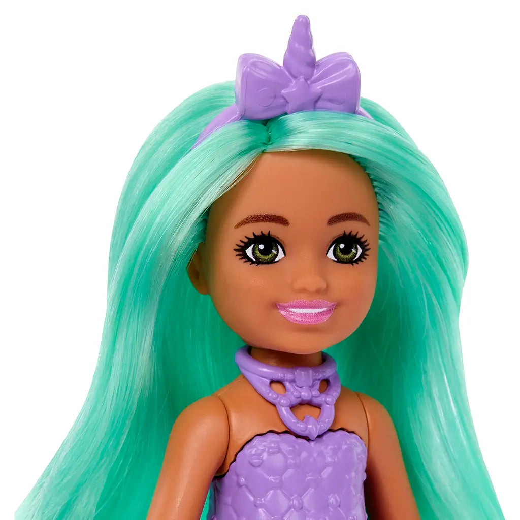 Close-up of Barbie Chelsea doll highlights her bright green hair, lavender unicorn headband, pink lipstick, and purple molded top with detailed unicorn necklace design.