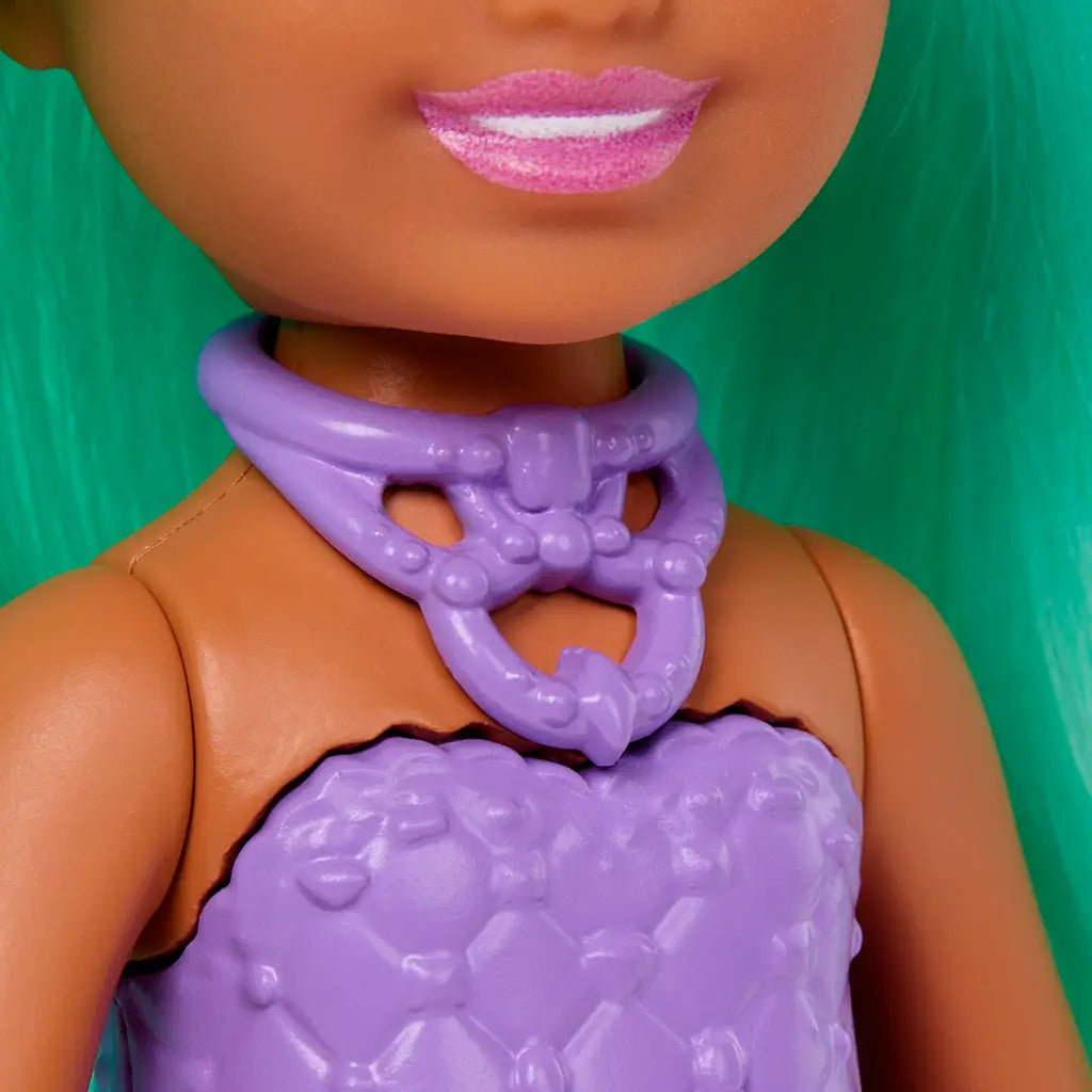 Close-up of Barbie Chelsea doll shows a molded lavender textured top with a purple unicorn necklace, paired with a colorful skirt and mint green hair cascading in the background.