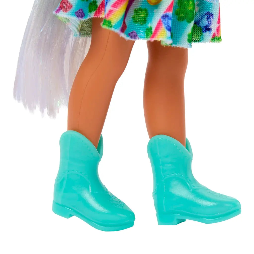 Close-up view of Barbie Chelsea doll’s turquoise cowboy-style boots paired with a colorful flared skirt decorated in rainbow prints, standing against white background.