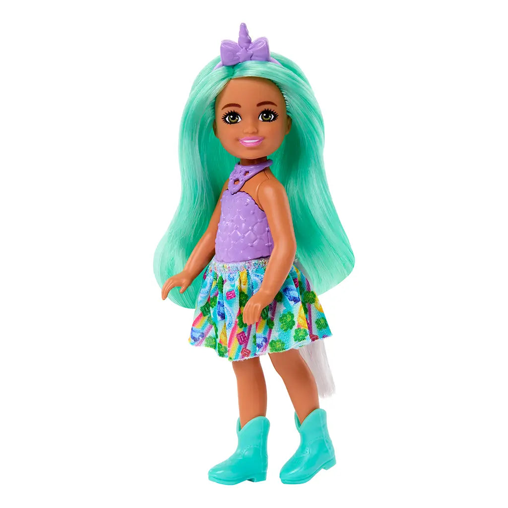 Barbie Chelsea doll with flowing mint green hair wears a lavender unicorn top, rainbow skirt, turquoise boots, and purple unicorn horn headband, standing on a white backdrop.