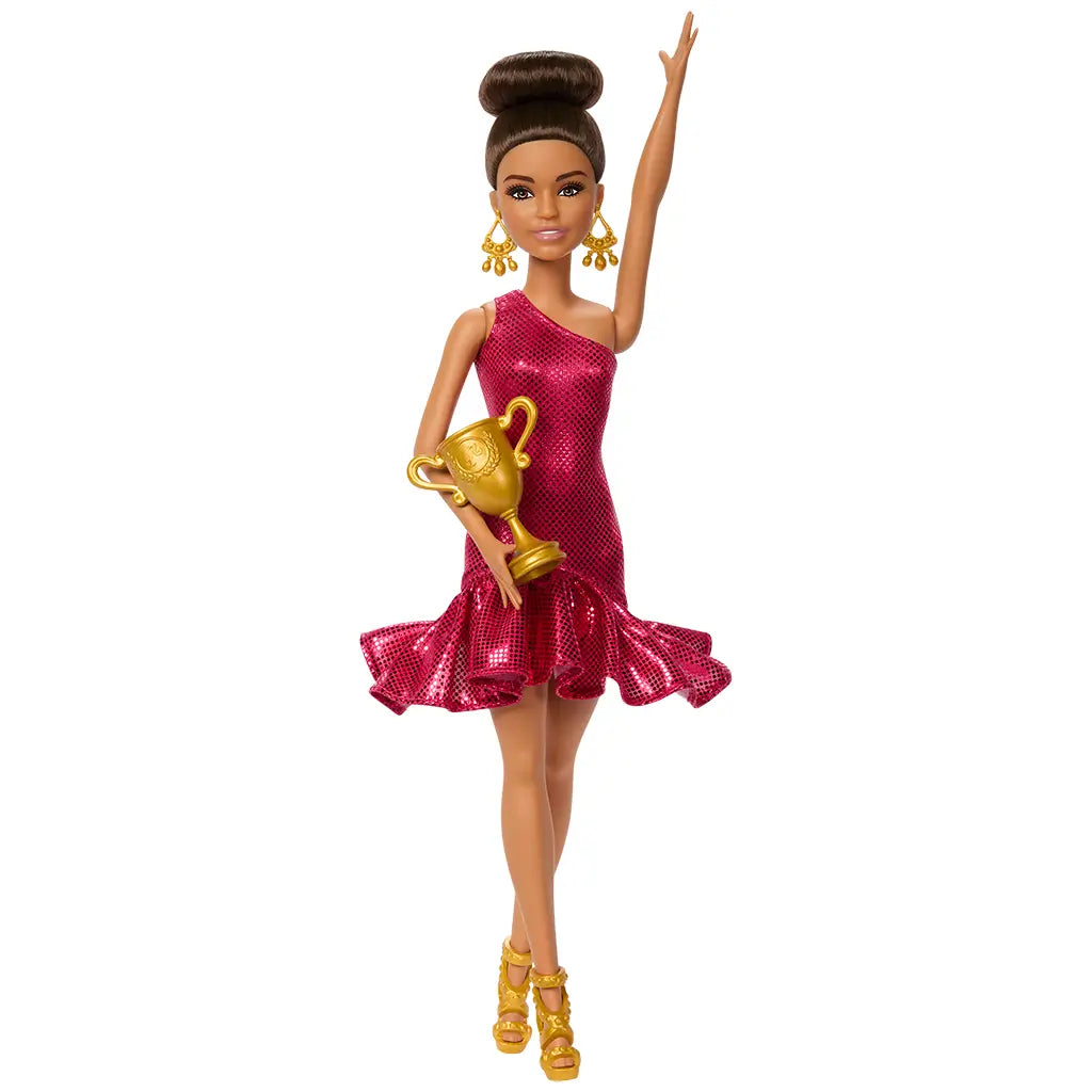 Barbie ballroom dancer doll in fuchsia one-shoulder dress raises one arm while holding a gold trophy, wearing gold heels and earrings.
