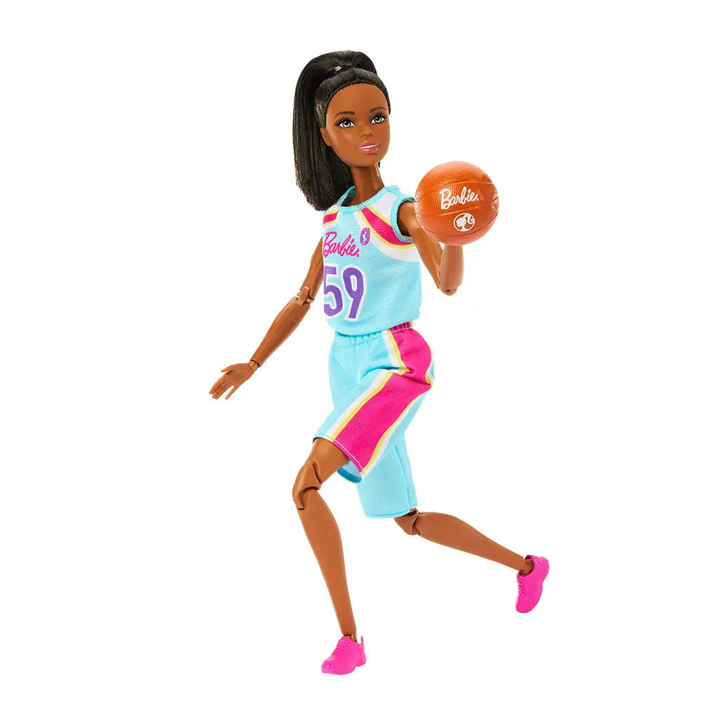 Barbie basketball player doll posed in a running motion, wearing a blue jersey with pink side panels and pink sneakers, holding a basketball mid-play with bendable joints.