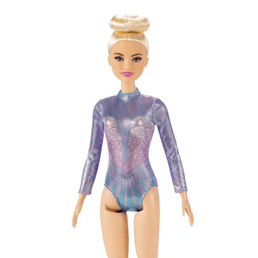 Close-up of Barbie rhythmic gymnast doll with blonde hair in a high bun, wearing a long-sleeved, shimmering purple and blue leotard with geometric details.