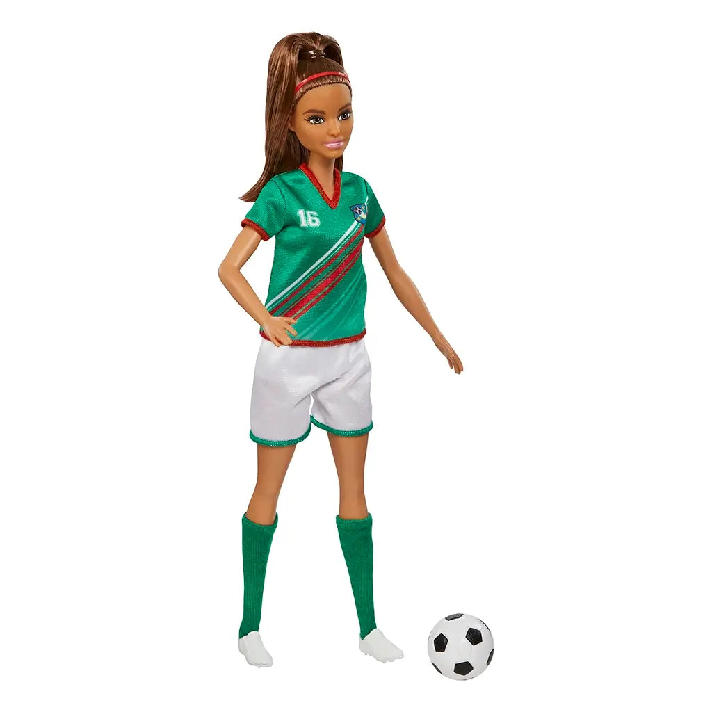 Barbie soccer player doll in green jersey with red accents, white shorts, and green socks, standing beside a black-and-white soccer ball, with long brown hair in ponytail.