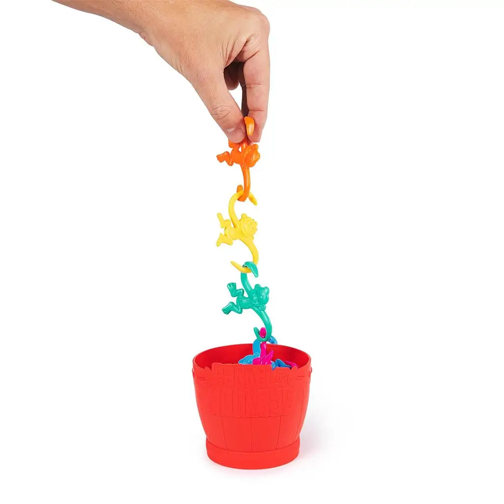 Hand lifting a chain of linked monkeys above the red Barrel of Monkeys container, demonstrating how to play by connecting curved monkey arms.
