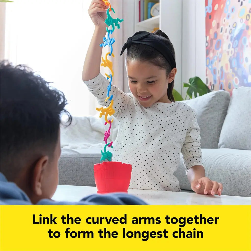 A young girl smiling as she lifts a long chain of colorful plastic monkeys from a red barrel while playing the Barrel of Monkeys game.