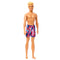 Angled front view of Beach Ken doll with blond hair and colorful purple geometric swim trunks, smiling and barefoot.
