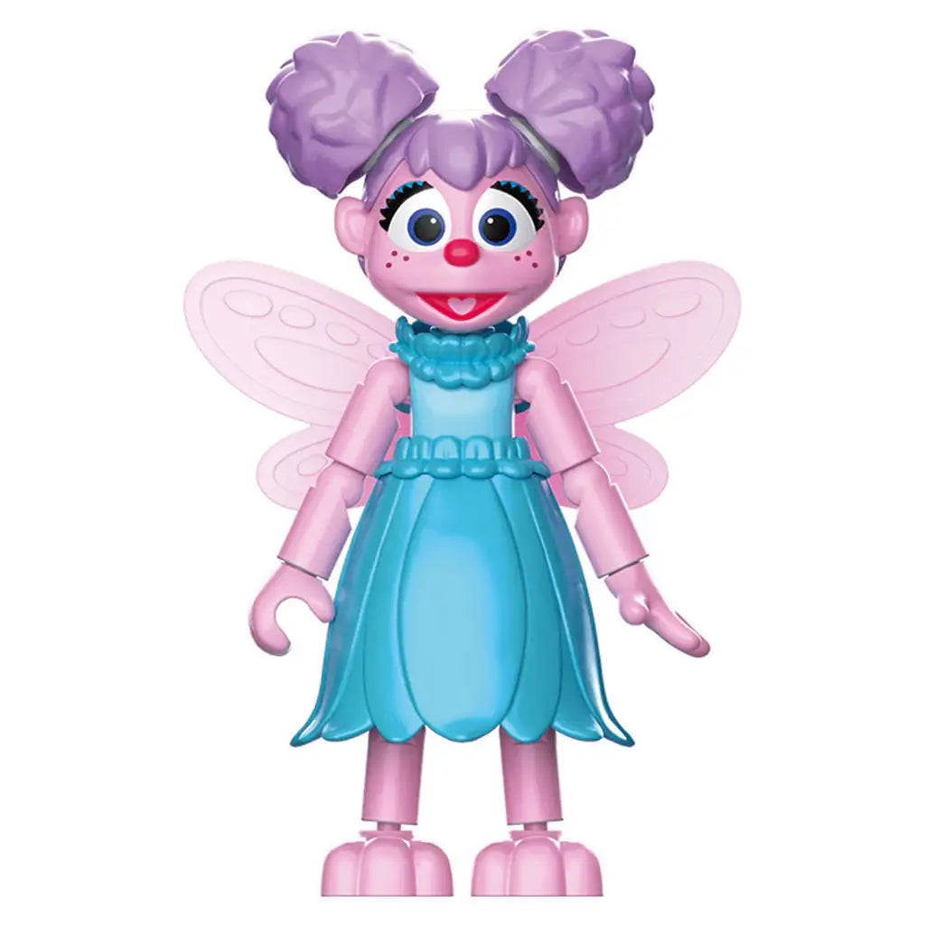 Pink and purple Abby Cadabby toy figure from Sesame Street with translucent fairy wings, big blue eyes, and a blue ruffled dress, standing on a white background with articulated limbs.