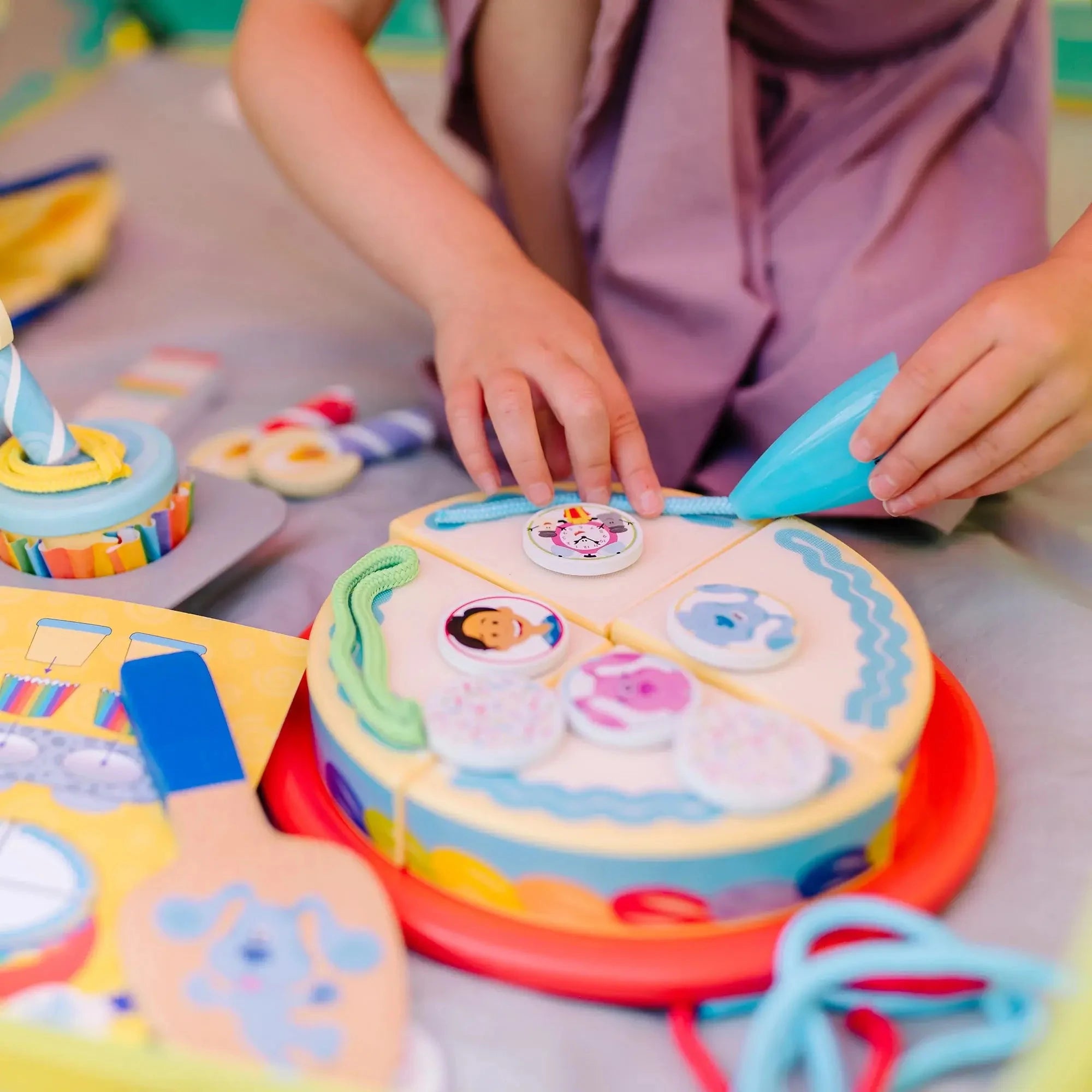 Child decorating wooden birthday cake pieces with Blue’s Clues characters and icing accessories, using a pretend piping tool for imaginative play.