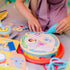 Child decorating wooden birthday cake pieces with Blue’s Clues characters and icing accessories, using a pretend piping tool for imaginative play.