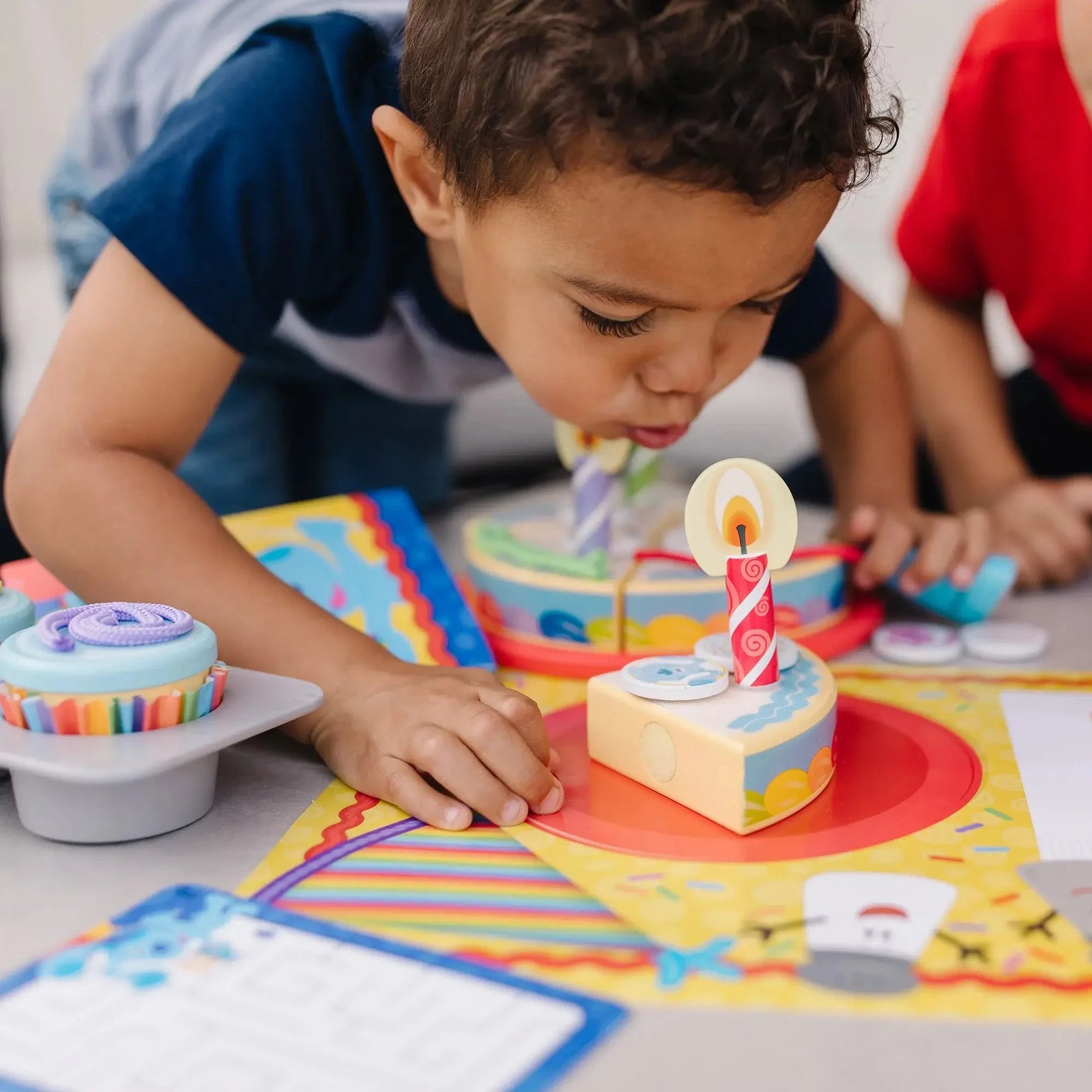 Child blowing out a wooden birthday candle on a pretend cake slice from the Blue’s Clues play set, surrounded by cupcakes and party-themed accessories.