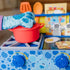 Child wearing a blue oven mitt while using a Blue’s Clues wooden stove toy with pretend food, red pot, and cooking accessories.