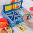 Child placing pretend food on a plate beside a Blue’s Clues wooden kitchen set with a red pot, utensils, sink, stove, and illustrated recipe card.