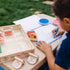 A young boy uses the Melissa & Doug Blue’s Clues & You! wooden handle stamps activity set outside, drawing and stamping Blue’s friends while building creativity and early literacy skills.