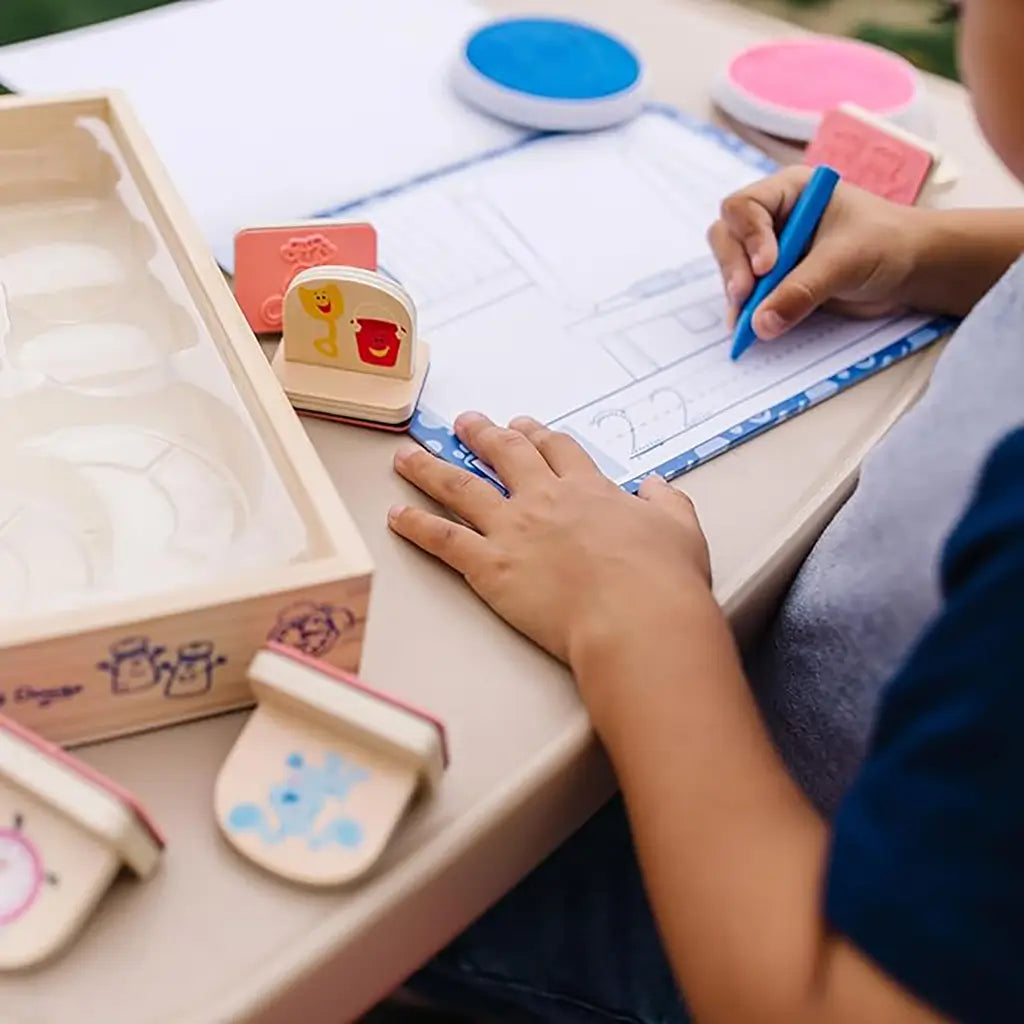 A young child uses the Melissa & Doug Blue’s Clues & You! wooden stamp set outdoors, tracing letters on a Blue’s Clues worksheet to build writing and coordination skills through creative hands-on fun.