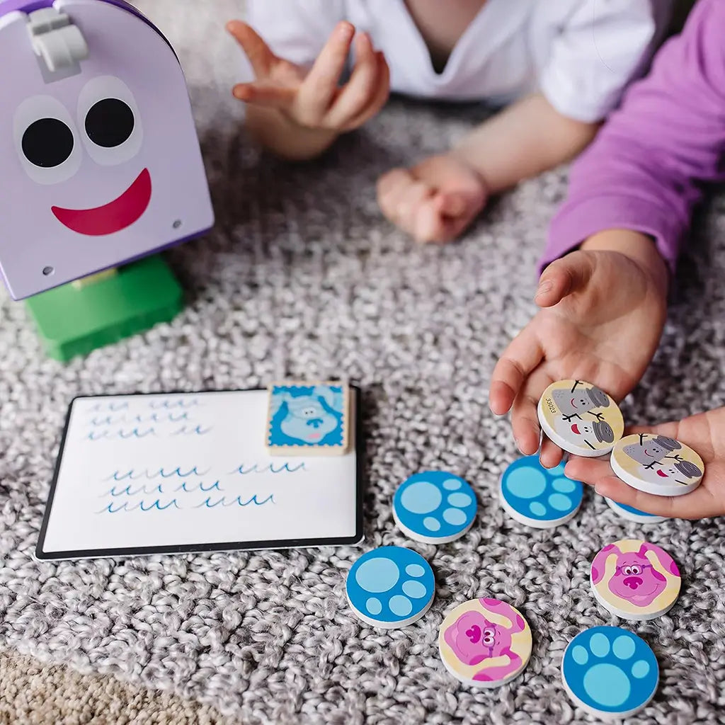 Two children play with Melissa & Doug Blue’s Clues & You! wooden mailbox set, matching illustrated wooden tokens featuring Blue and friends, fostering memory and storytelling skills through play.