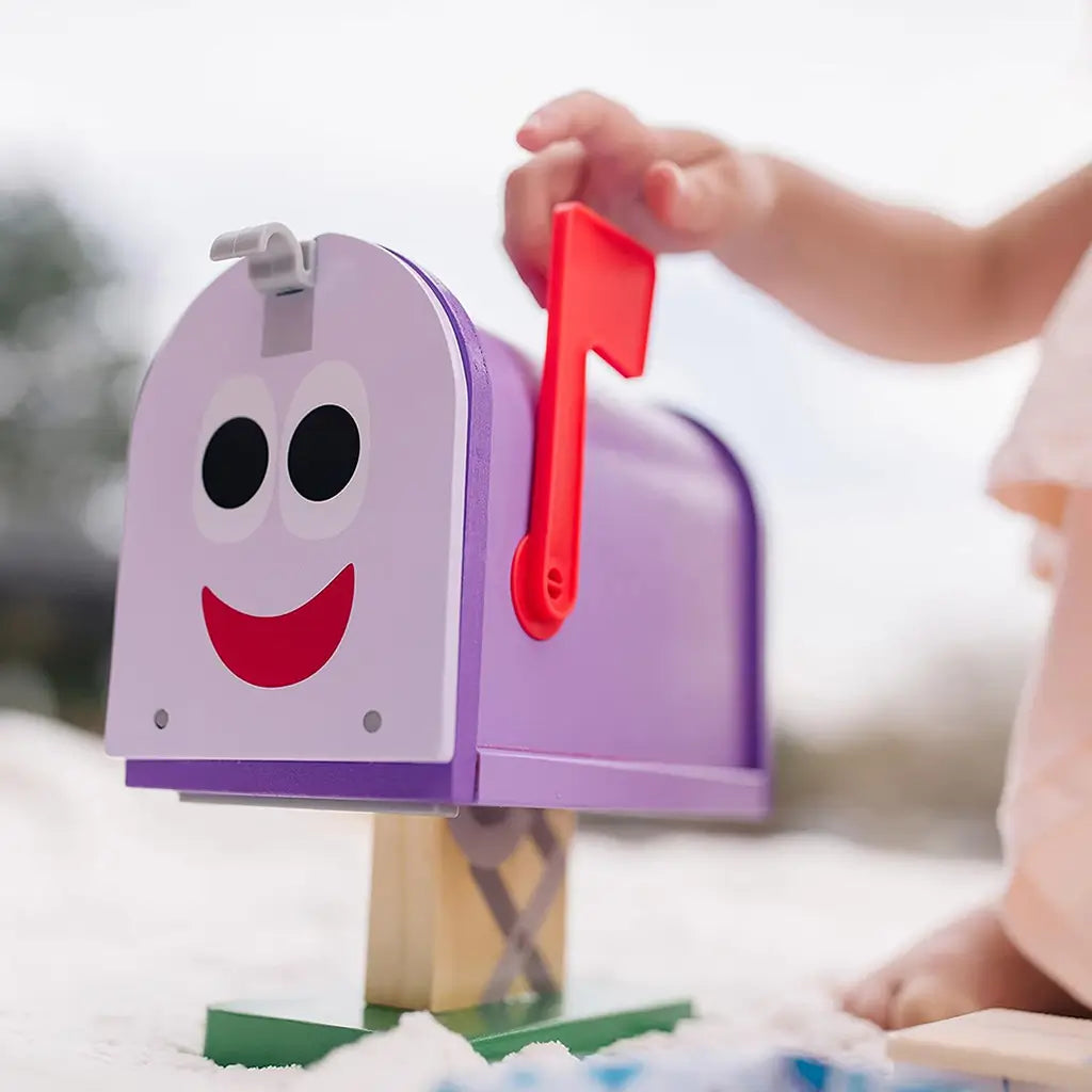 Close-up of Melissa & Doug Blue’s Clues & You! wooden mailbox play set showing a smiling purple mailbox with a red flag, encouraging imaginative mail-delivery play and role-playing creativity.