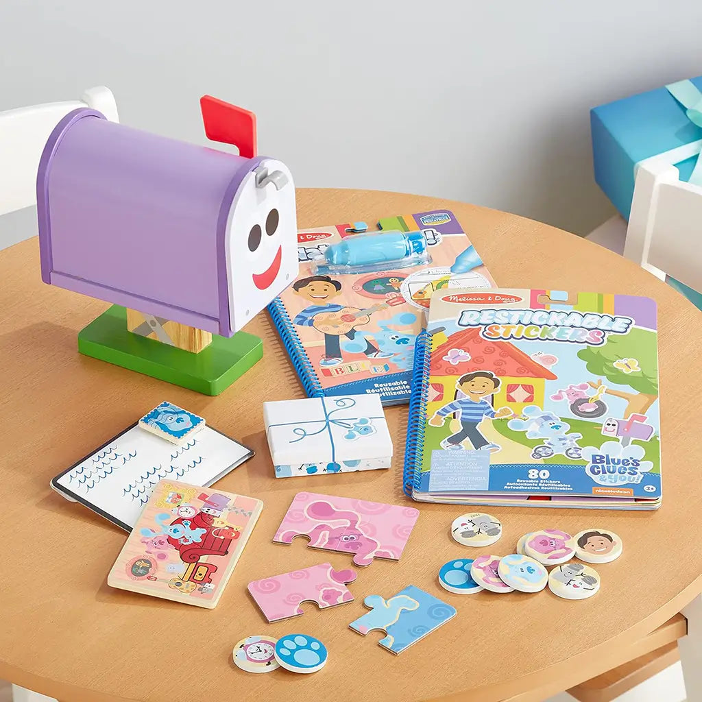 Melissa & Doug Blue’s Clues & You! mailbox play set displayed on a table with puzzles, sticker books, and letters, promoting fine motor skills and imaginative communication play for preschoolers.