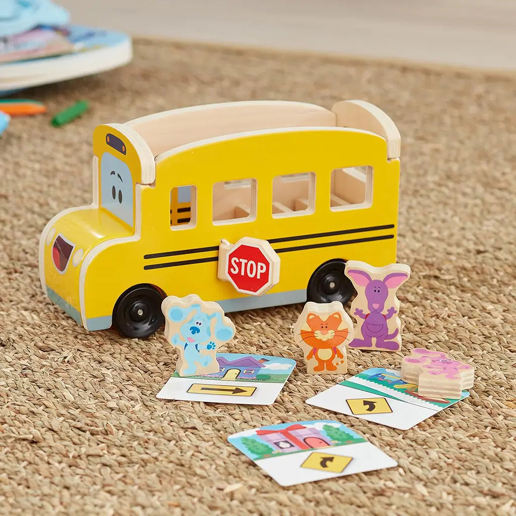 Melissa & Doug Blue’s Clues & You! wooden school bus toy with Blue, Magenta, and friends beside illustrated cards, promoting pretend play and storytelling while enhancing fine motor skills.