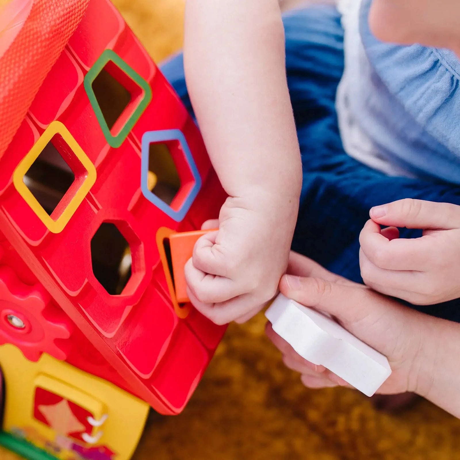 Close-up of toddler inserting a colorful shape into the sorter roof of the Blue’s Clues wooden take-along house toy during hands-on learning play.