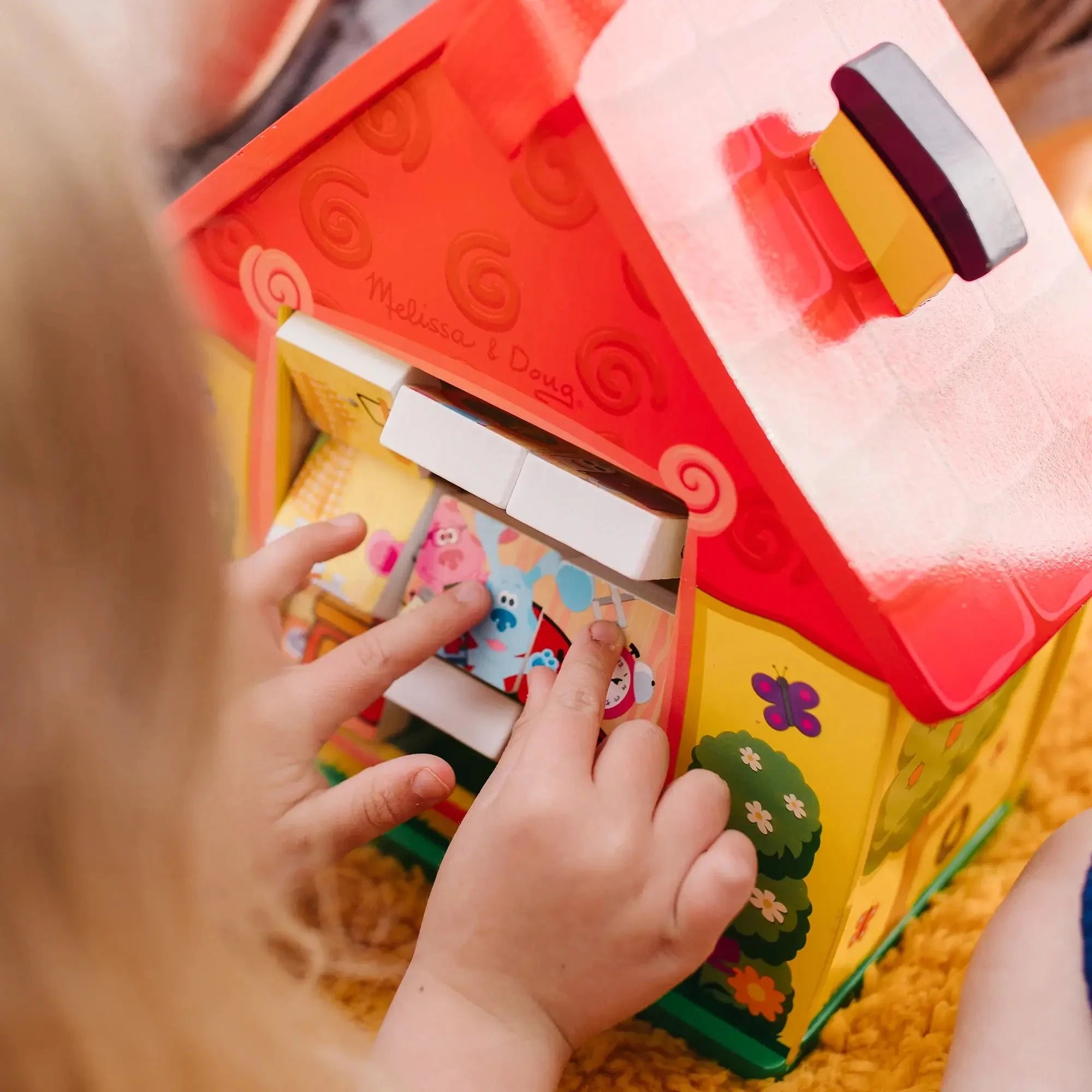 Child interacting with a Blue’s Clues wooden house puzzle, aligning blocks with character images, promoting fine motor and cognitive skills through play.