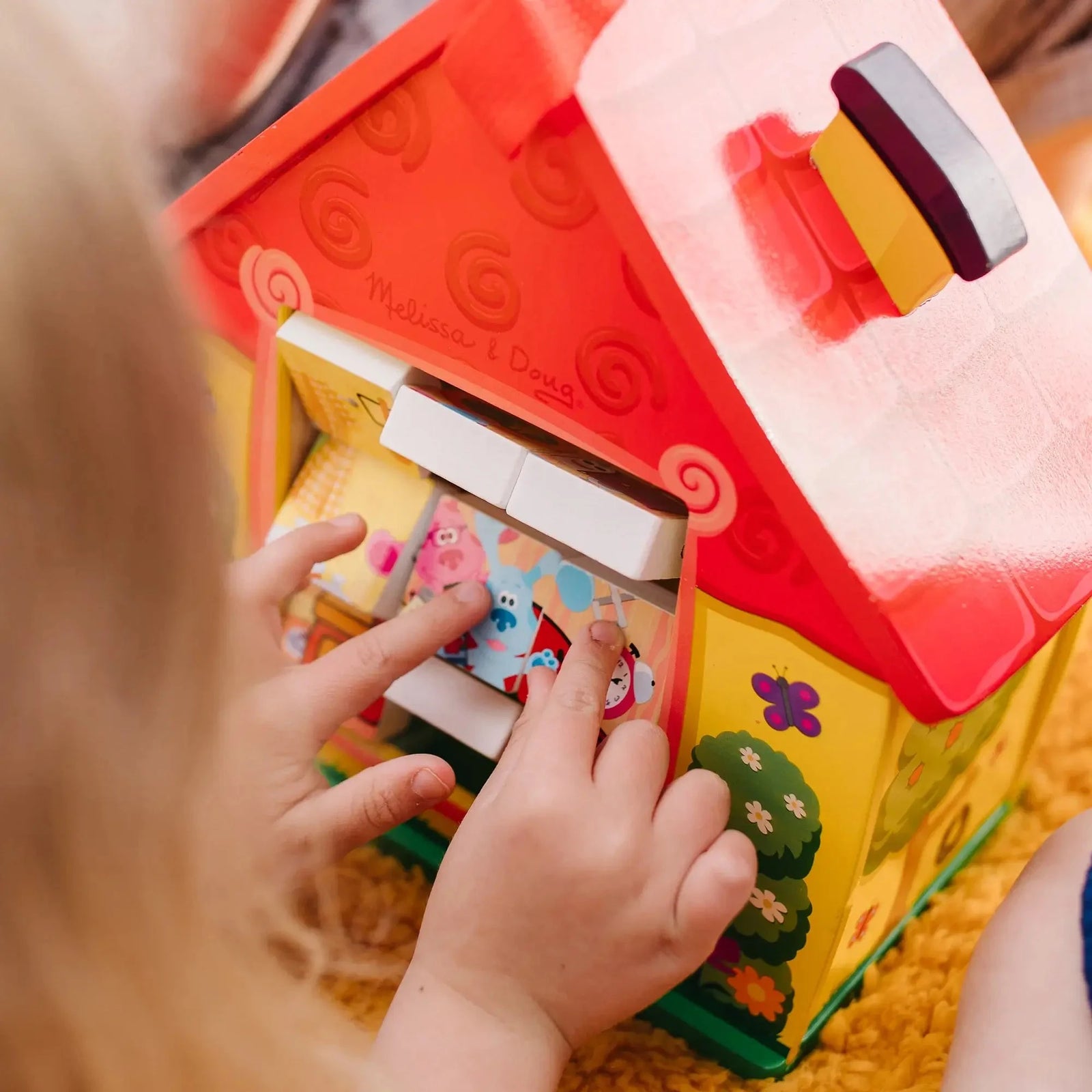 Child interacting with a Blue’s Clues wooden house puzzle, aligning blocks with character images, promoting fine motor and cognitive skills through play.