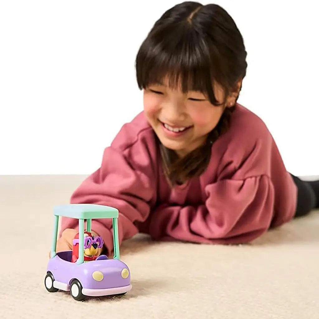 Young child playing on the floor with the Bluey Granny Car and Janet figure, showing interactive storytelling play and vehicle movement in a bright home setting.