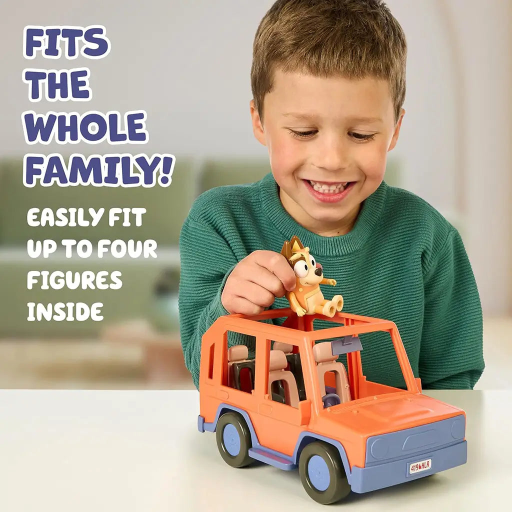 Child plays with Bluey Heeler 4WD vehicle, placing Chilli on the roof of the orange toy car that fits four figures, shown in a softly lit indoor room with subtle background shapes.