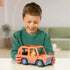 A smiling child holds the Bluey Heeler 4WD toy vehicle on a table, with Chilli seated inside the bright orange car, set in a cozy home environment with soft neutral background tones.