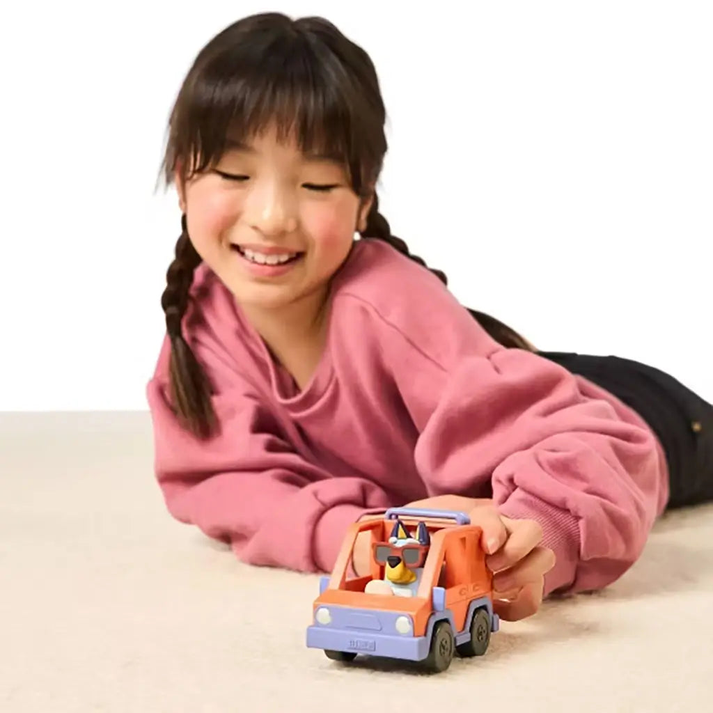 Child smiling while playing with the Bluey Mini 4WD vehicle and Bluey figure on the floor, demonstrating imaginative play.
