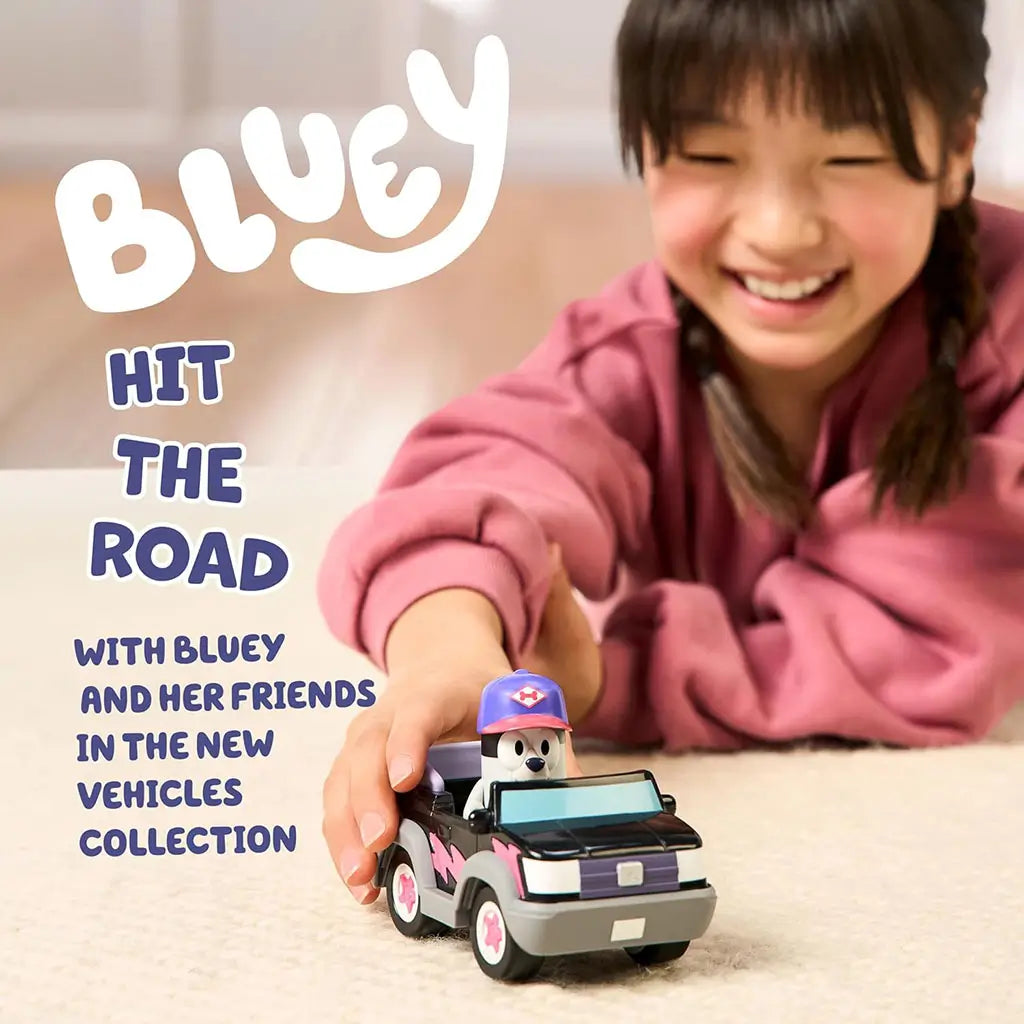 Bluey Muffin vehicle playset lifestyle image showing a smiling child pushing the black and gray convertible toy with Muffin figure seated inside, demonstrating hands-on play on a soft indoor floor.