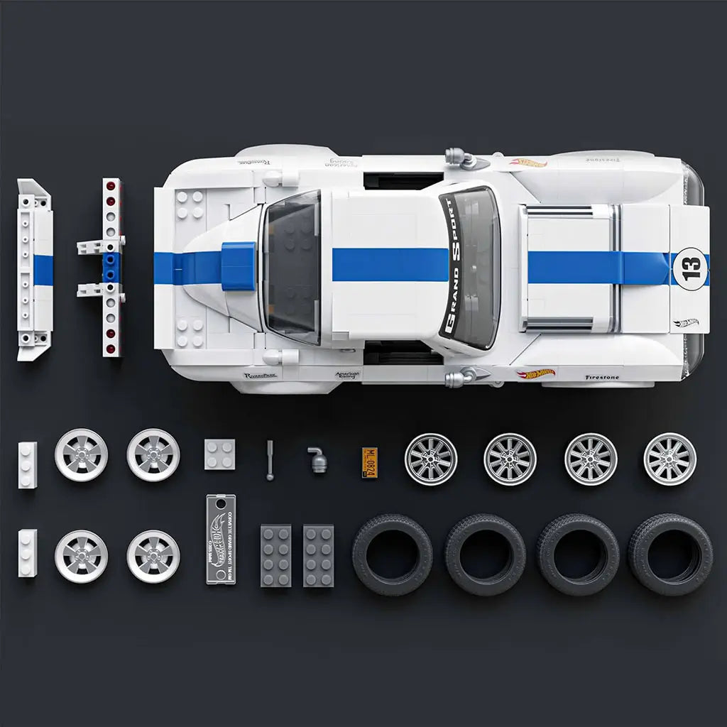 Hot Wheels Corvette Grand Sport building set parts laid out neatly, featuring white and blue plastic bricks, wheels, tires, accessories, and body panels arranged around the completed car on a dark surface.