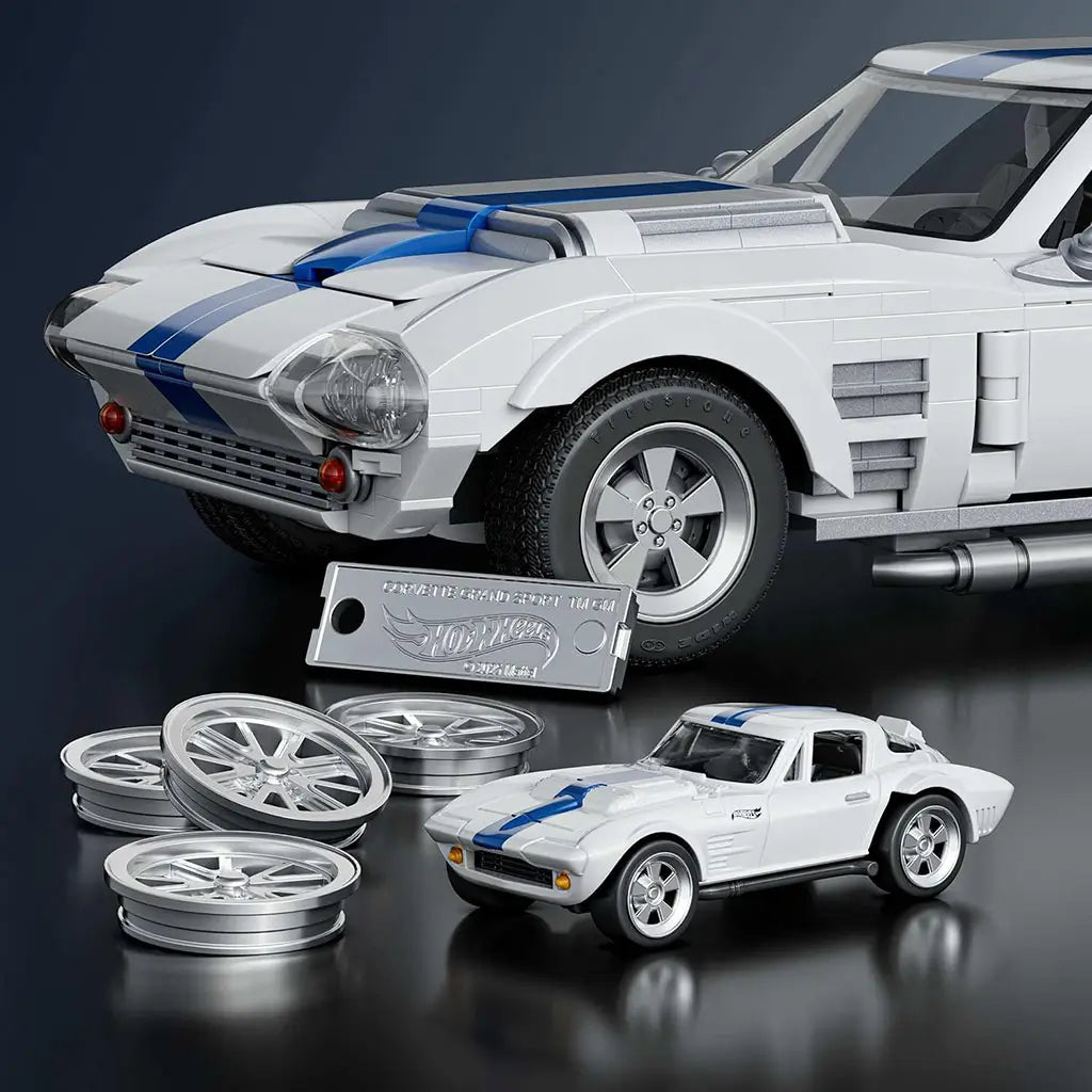 Hot Wheels Corvette Grand Sport set featuring white brick-built car with blue stripes, exclusive metal die-cast car, metal signature plate, and extra wheels displayed together on a reflective studio surface.