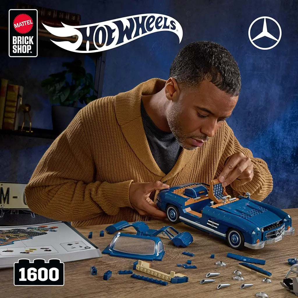 Adult builder assembling the Hot Wheels Mercedes-Benz 300 SL brick model in rich blue plastic, showing working gullwing doors, detailed interior pieces, loose components, and instruction booklet on a tabletop workspace.