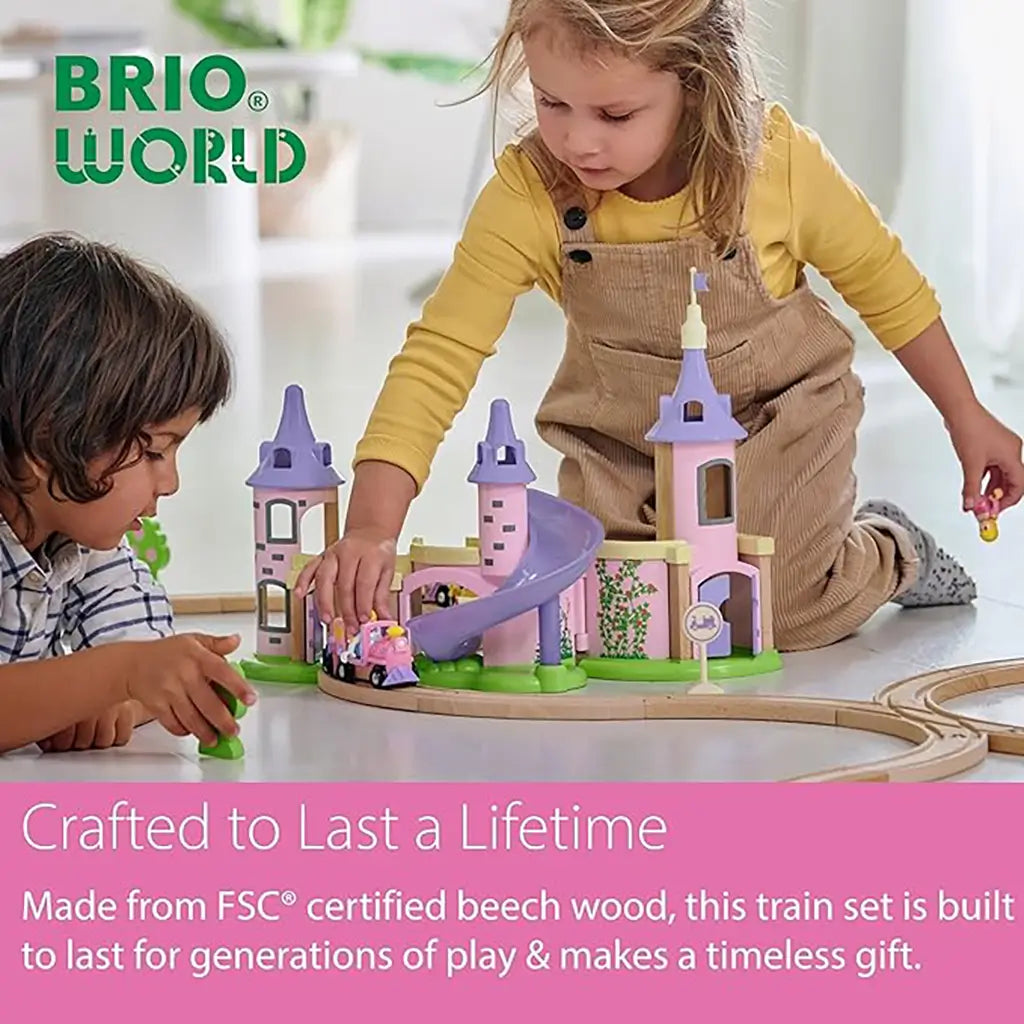 Two children playing with the BRIO Disney Princess Castle train set on the floor, featuring wooden tracks, pink train, and pastel castle with towers and glitter slide.