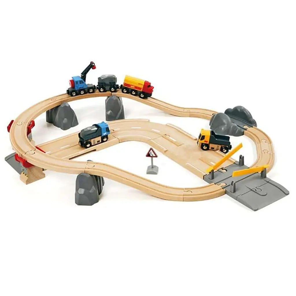 Wooden BRIO rail and road loading set with curved beech wood tracks, colorful toy trucks, cargo train, crane, and rocky scenery designed for imaginative quarry-themed play.