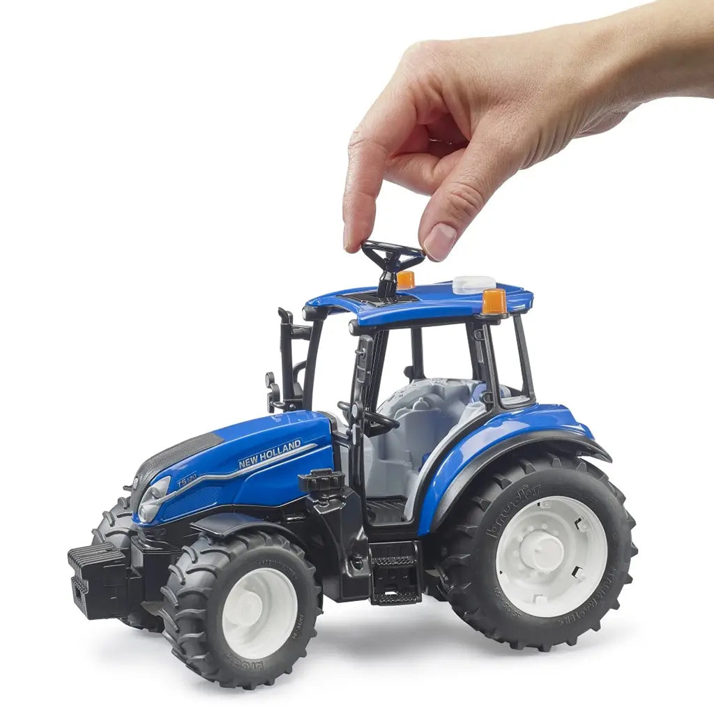 Hand adjusting steering wheel on Bruder New Holland T5 120 1:16 scale tractor, showcasing the interactive play feature and realistic farm vehicle design in blue and black plastic.