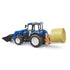 Blue New Holland T5.120 toy tractor with black loader arm lifting attachment and yellow hay bale in front grip, set on a white background showcasing realistic miniature farm vehicle design and detail.
