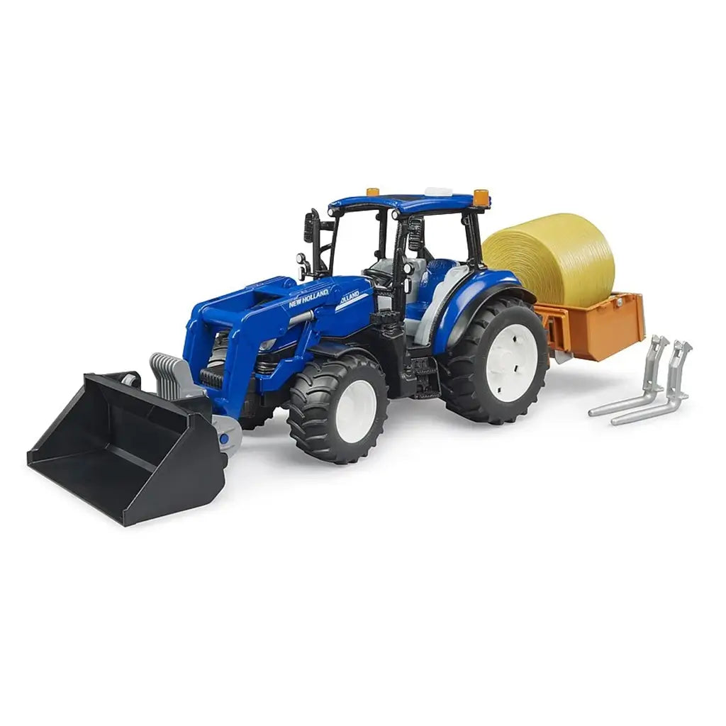 Blue New Holland T5.120 model tractor with front loader, orange rear trailer carrying yellow hay bale, and detachable silver fork attachments, positioned on a white surface for toy farm collection display.
