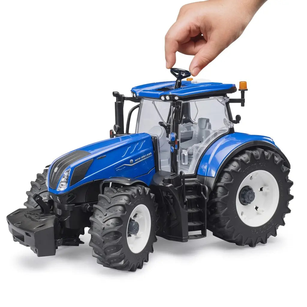 Bruder 1:16 scale New Holland T7.340 toy tractor with steerable front axle, shown with a hand using the roof-mounted steering rod.