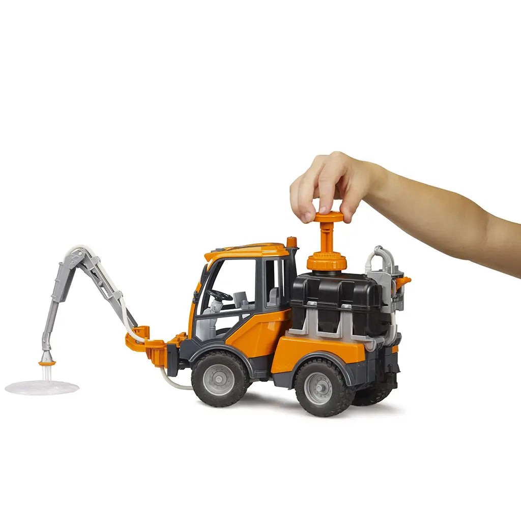BRUDER VarioCar irrigation toy features orange, black, and gray plastic construction with a hand operating the tank pump while the articulated sprinkler arm dispenses water.