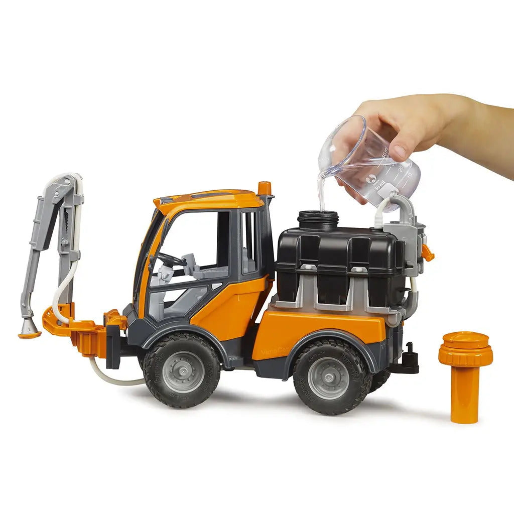 BRUDER VarioCar irrigation toy features orange, black, and gray plastic construction as a hand pours water into the fillable rear tank, with the orange cap set beside it.