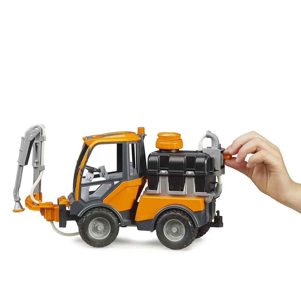 BRUDER VarioCar irrigation toy features orange, black, and gray plastic construction with a rear water tank and pump control being turned by hand beside the detailed cab.