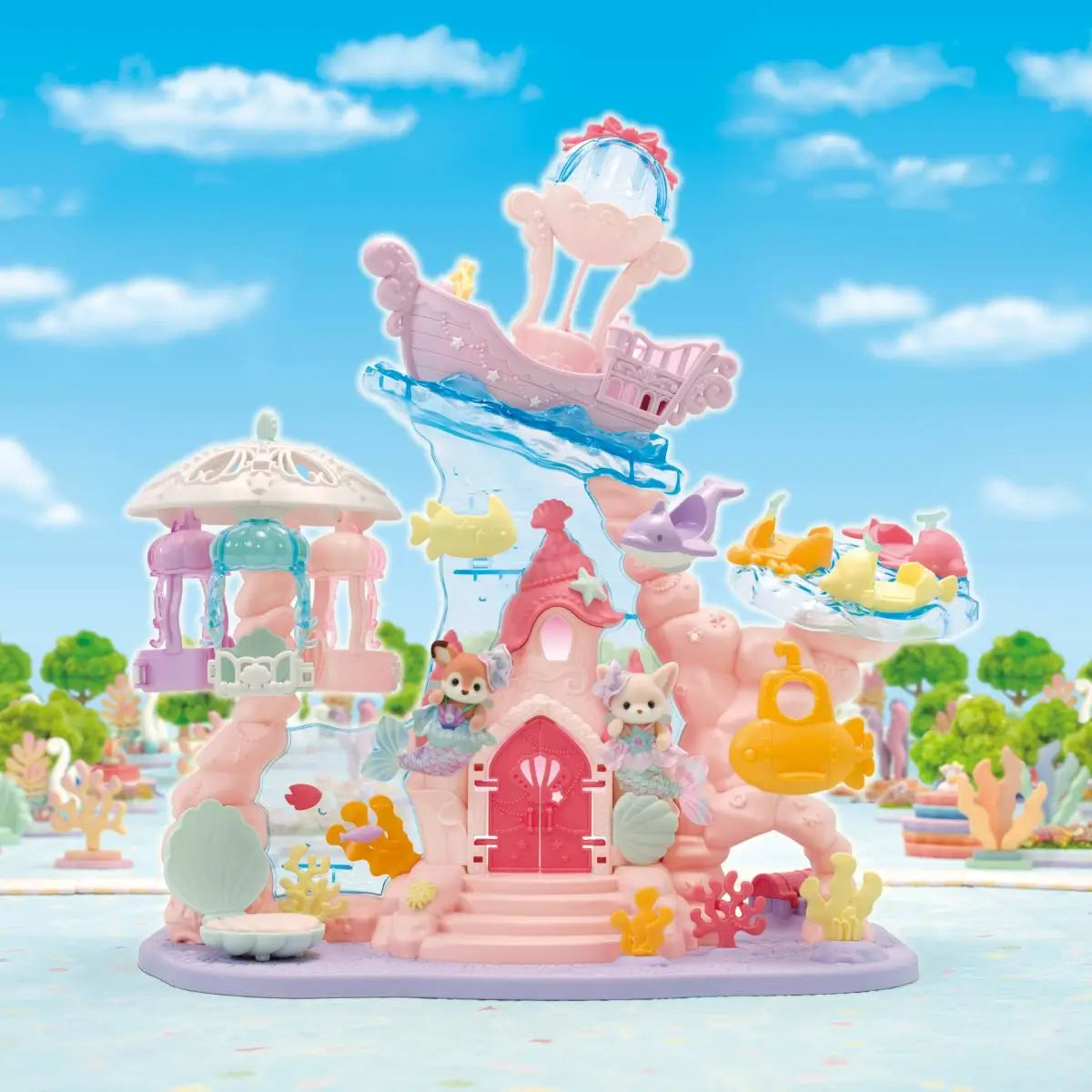Calico Critters Baby Mermaid Castle playset features pastel pink and lavender plastic castle with blue wave slide, shell details, carousel ride, and small animal figures in underwater themed park setting.