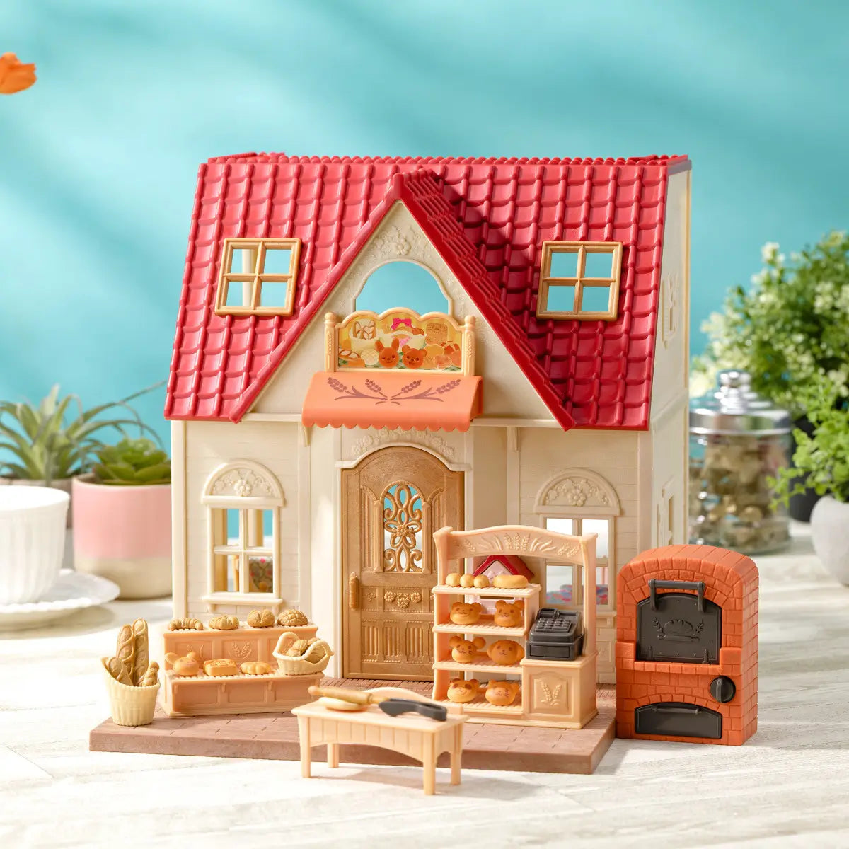 Calico Critters bakery shop display with cream cottage, red shingled roof, brick oven, bread stand, prep table, and miniature baked goods arranged on tabletop background.