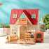 Calico Critters bakery shop display with cream cottage, red shingled roof, brick oven, bread stand, prep table, and miniature baked goods arranged on tabletop background.