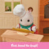 Calico Critters bakery oven feature in orange brick-textured plastic with pullout gray tray holding animal-shaped bread roll, shown baking inside miniature kitchen wall setting.
