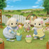 Calico Critters toy set shows soft cream-colored rabbit figures in blue gingham outfits tending tulips with a watering can in a grassy garden scene with a white fence.