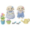 Calico Critters toy set includes two cream rabbit figures in blue gingham outfits, tulip flowers in pots, gardening tools, and a yellow watering can arranged neatly.